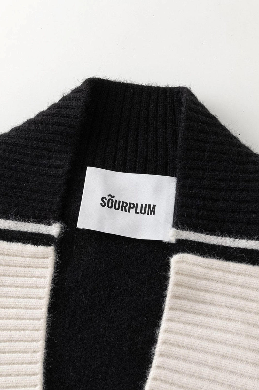 Close up product detail of color block knit V-neck racing stripe sweater collar and ribbed neckline
