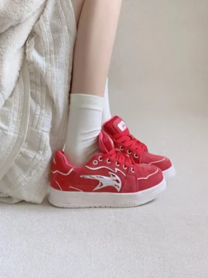 Burgundy low-top skate sneakers worn with white socks, featuring contrast white side logos and clean white rubber soles in a casual streetwear setting