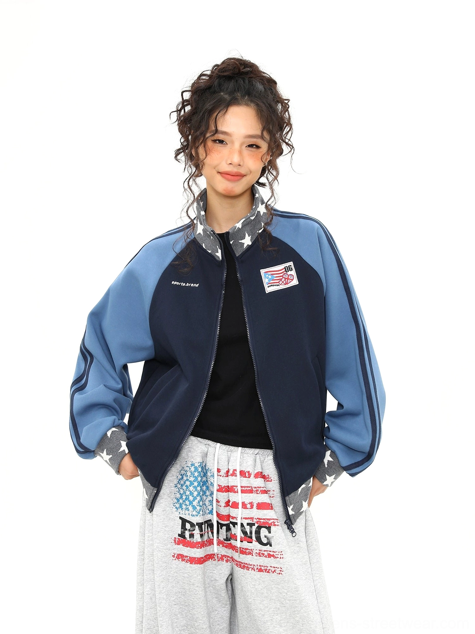Front view of a colorblock varsity track jacket with hands in pockets, star print hem, chest graphic, and grey sweatpants
