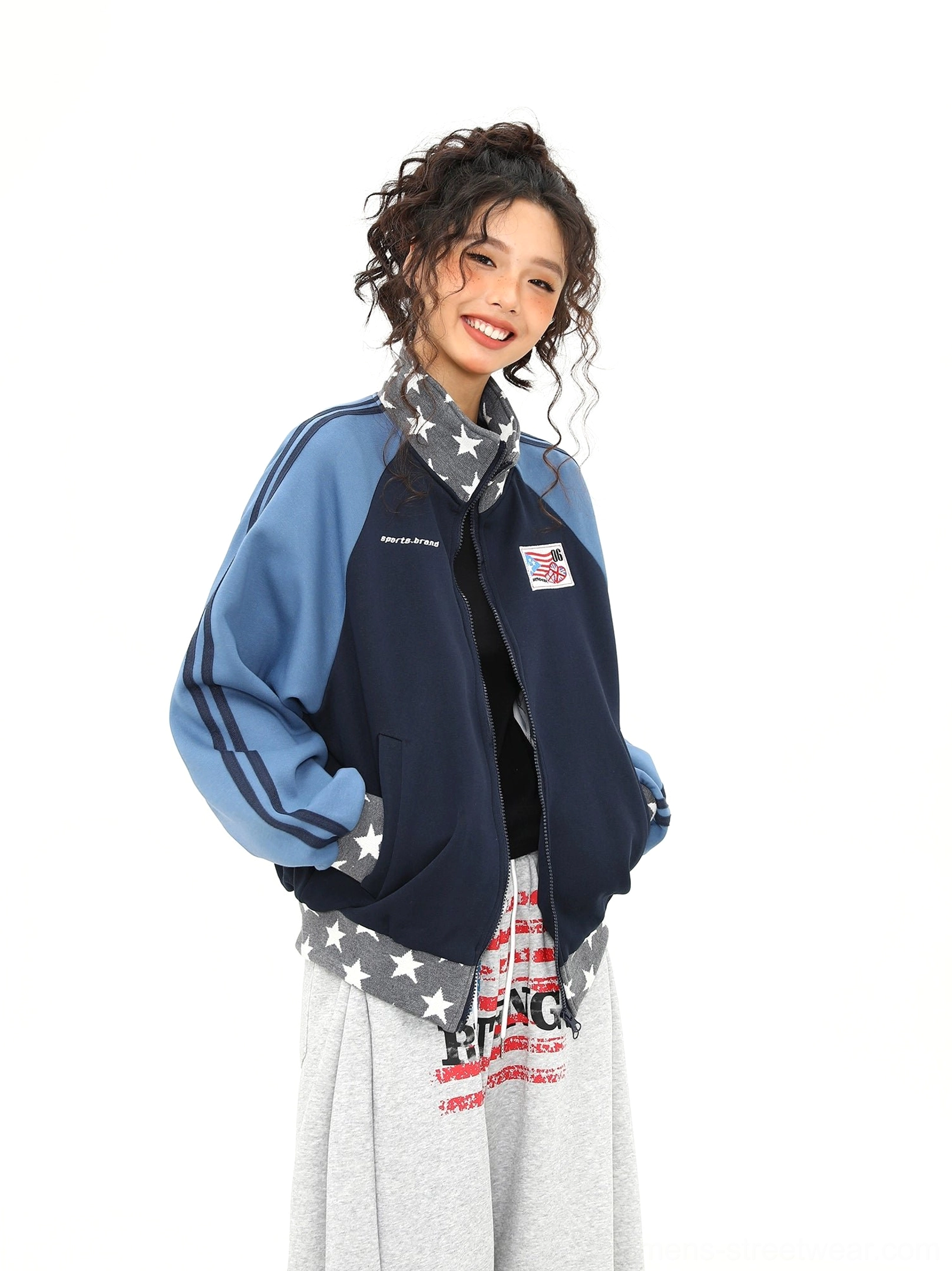 Side three quarter view of a cropped navy and blue varsity track jacket with striped raglan sleeves and star print trim
