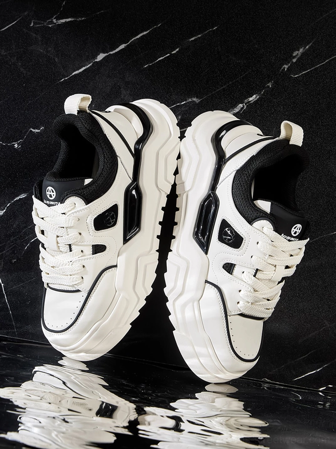 Black and white cutout platform sneakers displayed on a reflective black marble surface
