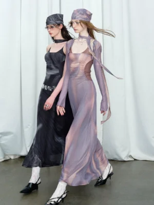 Two women wearing black and dusty purple contrast mesh satin maxi dresses with sheer sleeves, floor-length silhouettes, head wraps, and streetwear styling