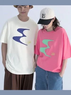 Two models wearing oversized contrast patch logo streetwear tees in hot pink and off-white with wavy graphic designs, wide-leg pants, and casual streetwear accessories