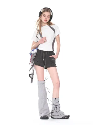 White and gray contrast shoulder cropped baby tee styled with black shorts and gray leg warmers in a minimalist streetwear studio look