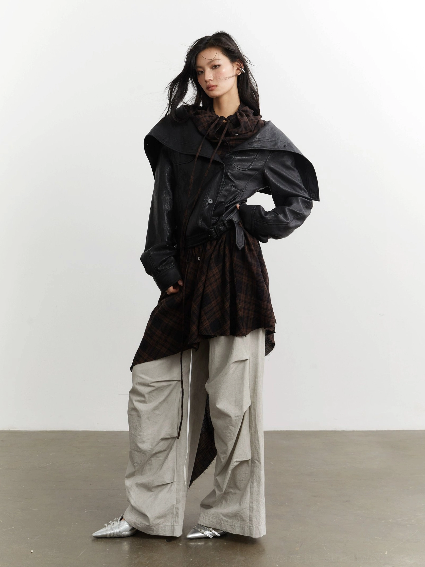 Front three-quarter view of a convertible black faux leather jacket with drawstring collar asymmetric plaid panel and cargo streetwear styling
