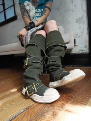 Model wearing convertible distressed canvas knee-high buckle boots with layered punk streetwear outfit indoors