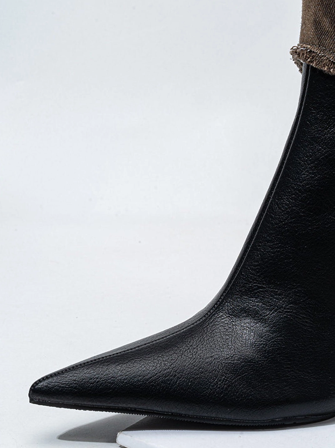 Close-up of pointed toe and slim stiletto heel on black statement boots for Y2K streetwear outfits