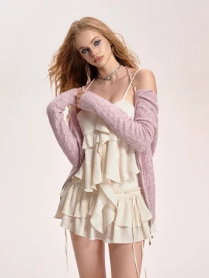 Pink convertible halter-neck cropped knit cardigan styled over an ivory ruffle mini dress in a minimalist studio