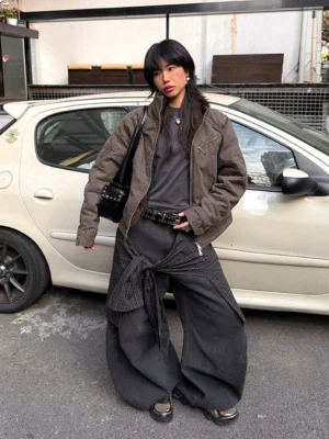 Female model wearing dark washed convertible plaid overlay barrel jeans with ultra wide legs in an outdoor streetwear setting