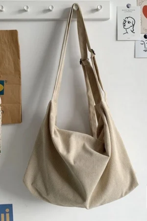 Off white corduroy slouchy crossbody bag with ribbed texture and long shoulder strap hanging on wall