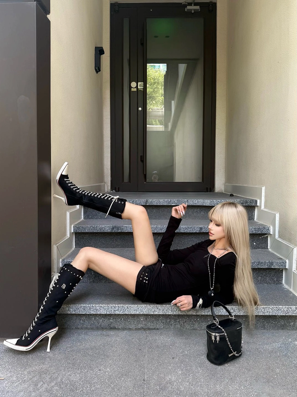 Side view of black corset lace-up knee-high stiletto boots styled with black shorts and a fitted streetwear top
