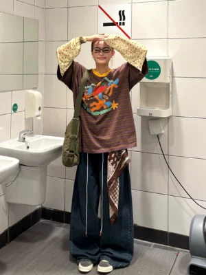 Brown striped fake two-piece graphic long sleeve tee styled with wide leg jeans and crossbody bag, featuring retro cartoon artwork and yellow contrast collar