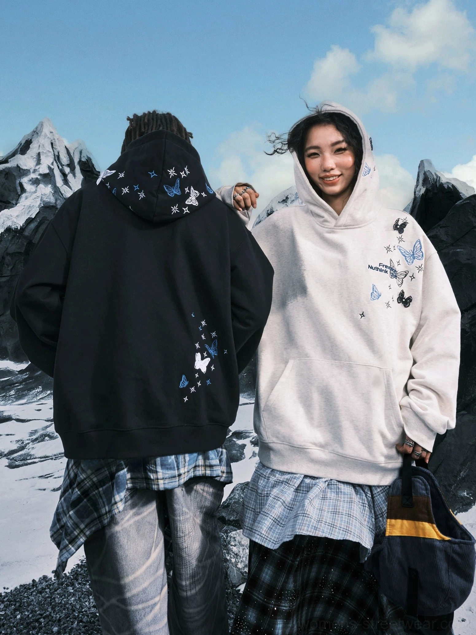 Couple streetwear styling featuring Black and White Ash oversized hoodies with butterfly embroidery in a snowy outdoor scene