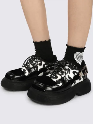 Front close-up of cow print platform Mary Jane shoes styled with black ruffled heart-detail socks and chunky elevated soles