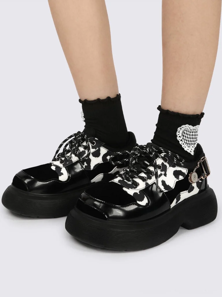 Front close-up of cow print platform Mary Jane shoes styled with black ruffled heart-detail socks and chunky elevated soles