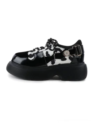 Cow print platform Mary Jane shoes with glossy black toe caps, lace-up vamp, side buckle strap, and chunky black platform sole on a light gray background