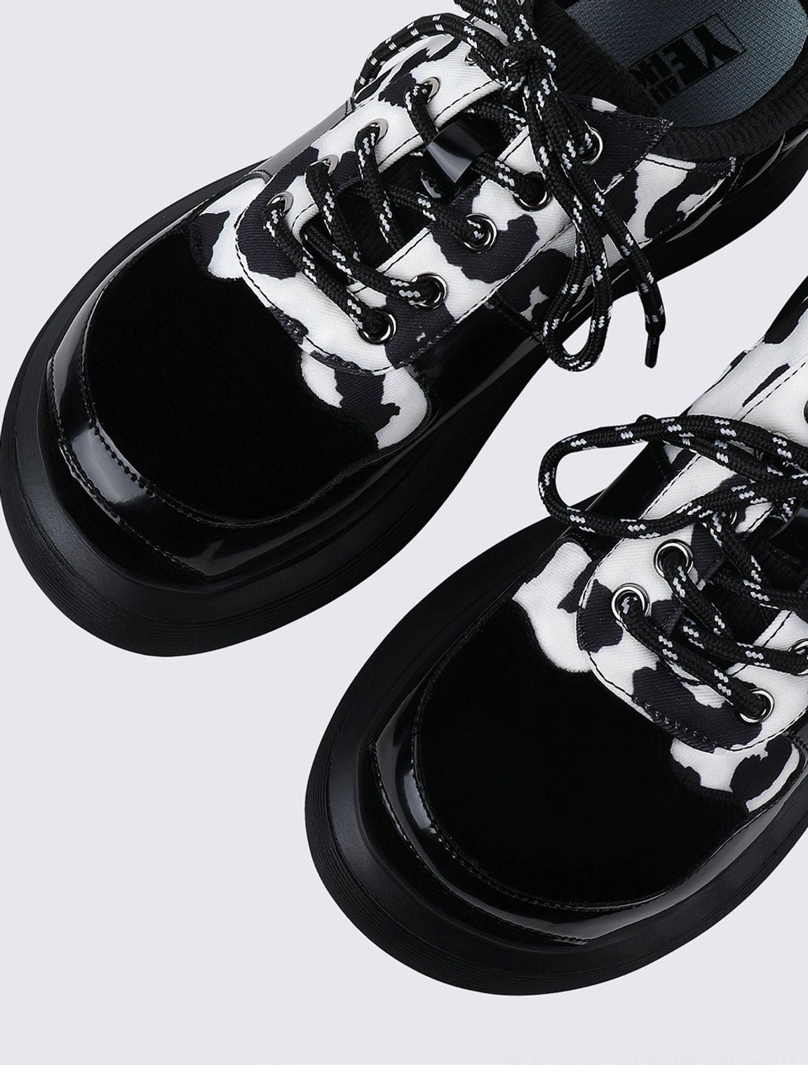 Cow print platform Mary Jane shoes with buckle straps, lace-up detailing, glossy black accents, and chunky elevated soles