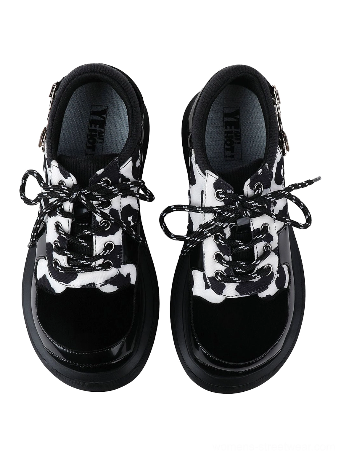 Pair of cow print platform lace-up Mary Jane shoes shown from the front with contrast laces, side buckles, and glossy toe caps