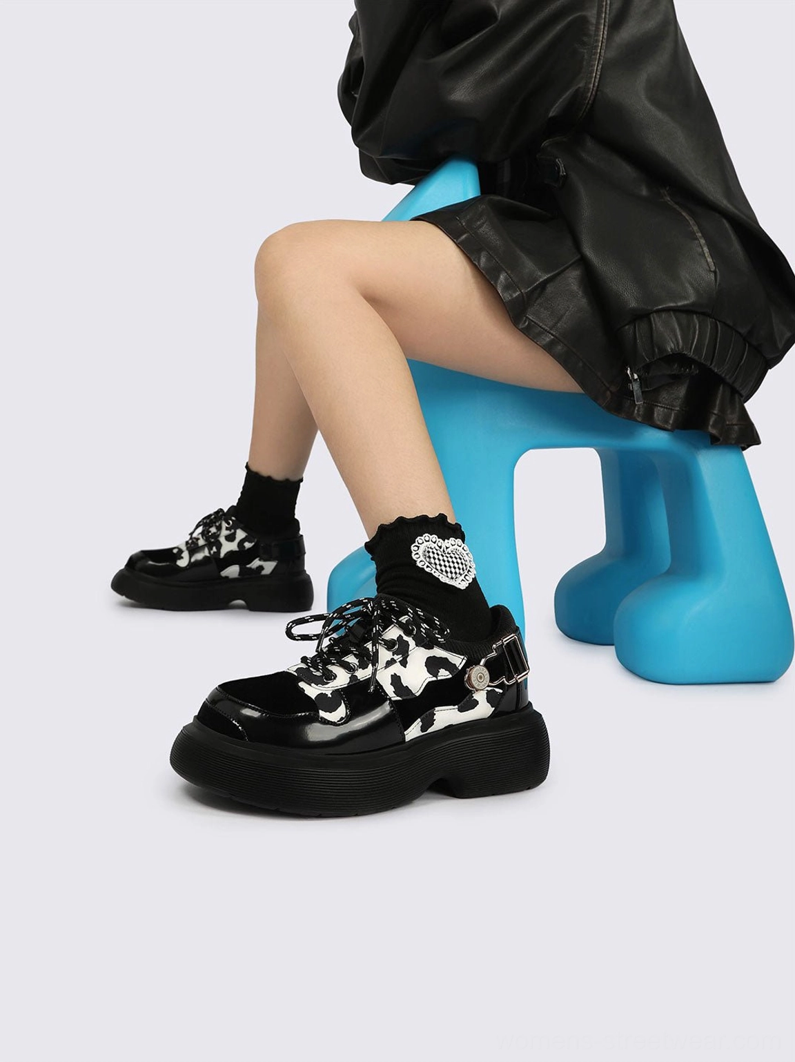 Side and back view of cow print platform Mary Jane shoes styled with a black leather jacket, skirt, and decorative buckle details