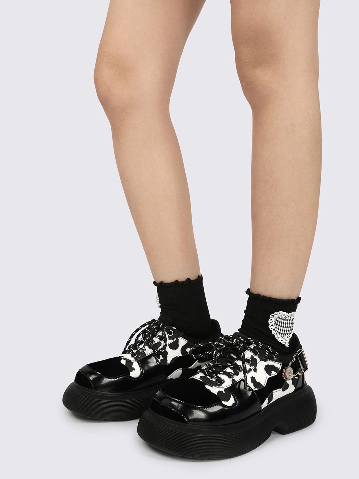 Front view of a pair of cow print platform Mary Jane shoes with polished black toe caps, matching laces, and chunky soles