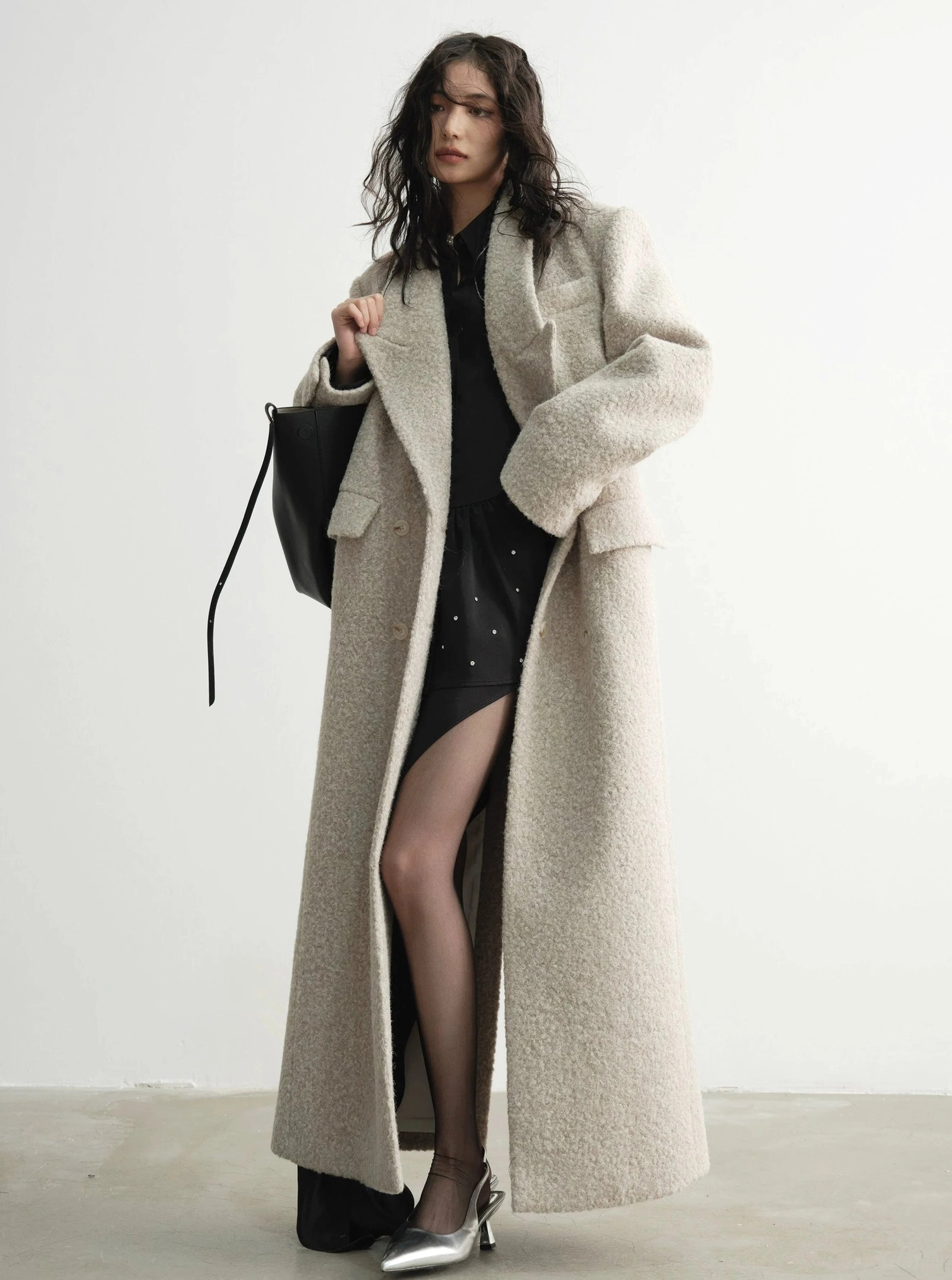 Creamy beige oversized floor-length wool coat styled with sheer black stockings and silver heels for an elegant streetwear look