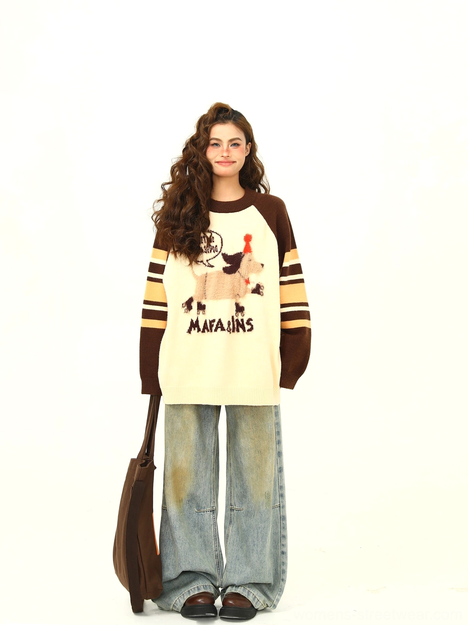 Full-body styling of a cream and brown oversized animal graphic knit sweater with striped sleeves and relaxed streetwear jeans