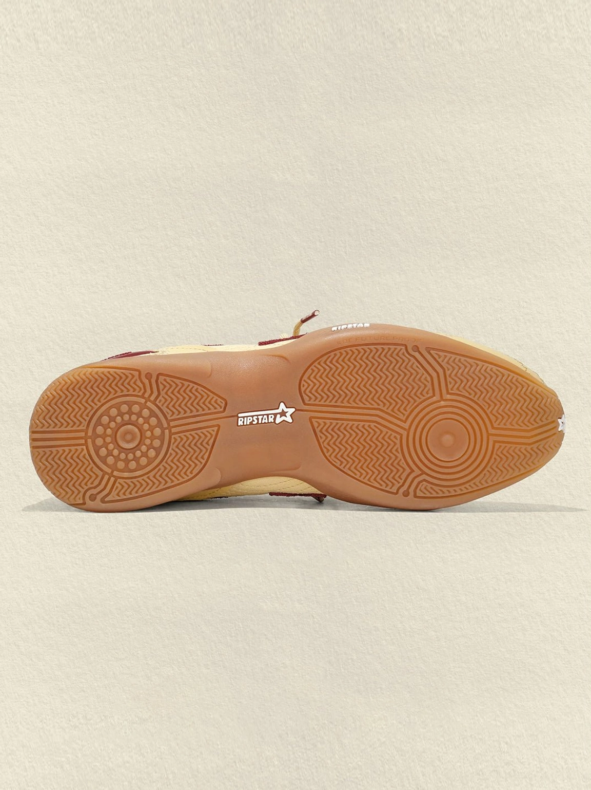 Close-up of cream burgundy star retro running sneaker outsole with circular anti-slip tread and center star logo