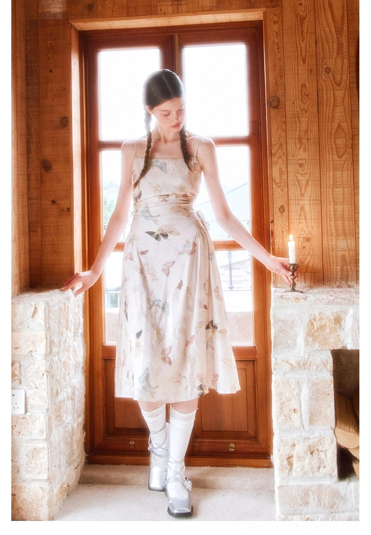 Cream butterfly print square neck spaghetti strap dress shown on a model beside a rustic wooden cabin window