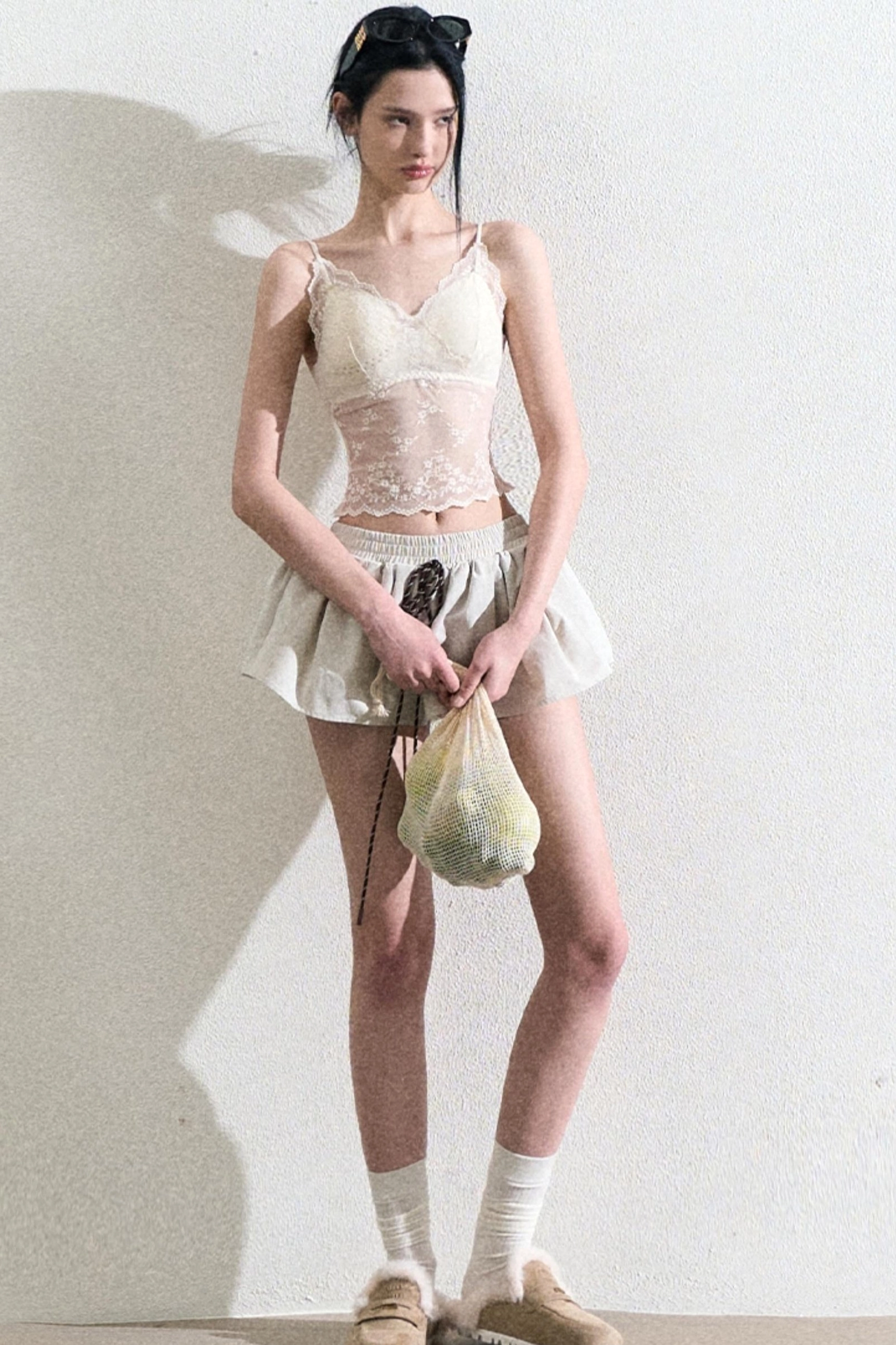 Front view of a cream camisole top and flowy mini skirt styled with a casual mesh bag