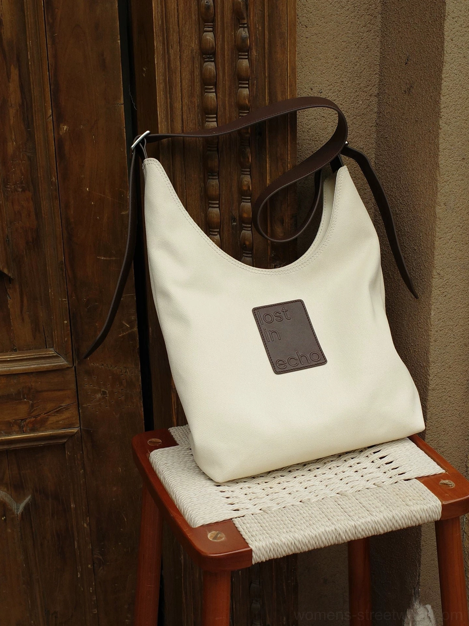 Cream canvas hobo commuter tote bag with dark brown leather shoulder straps displayed against a vintage wooden background