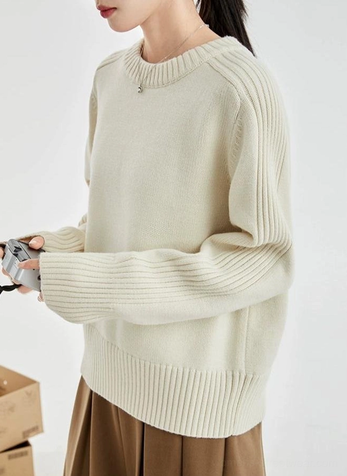 Side front view of a cream drop-shoulder knit sweater with ribbed sleeves styled with a pleated skirt and vintage film camera
