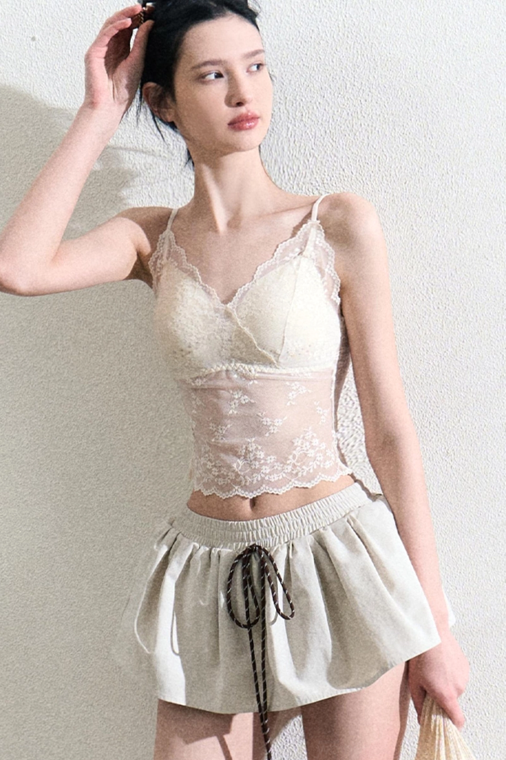 Side view of a cream floral lace camisole top styled with a ruffled drawstring mini skirt
