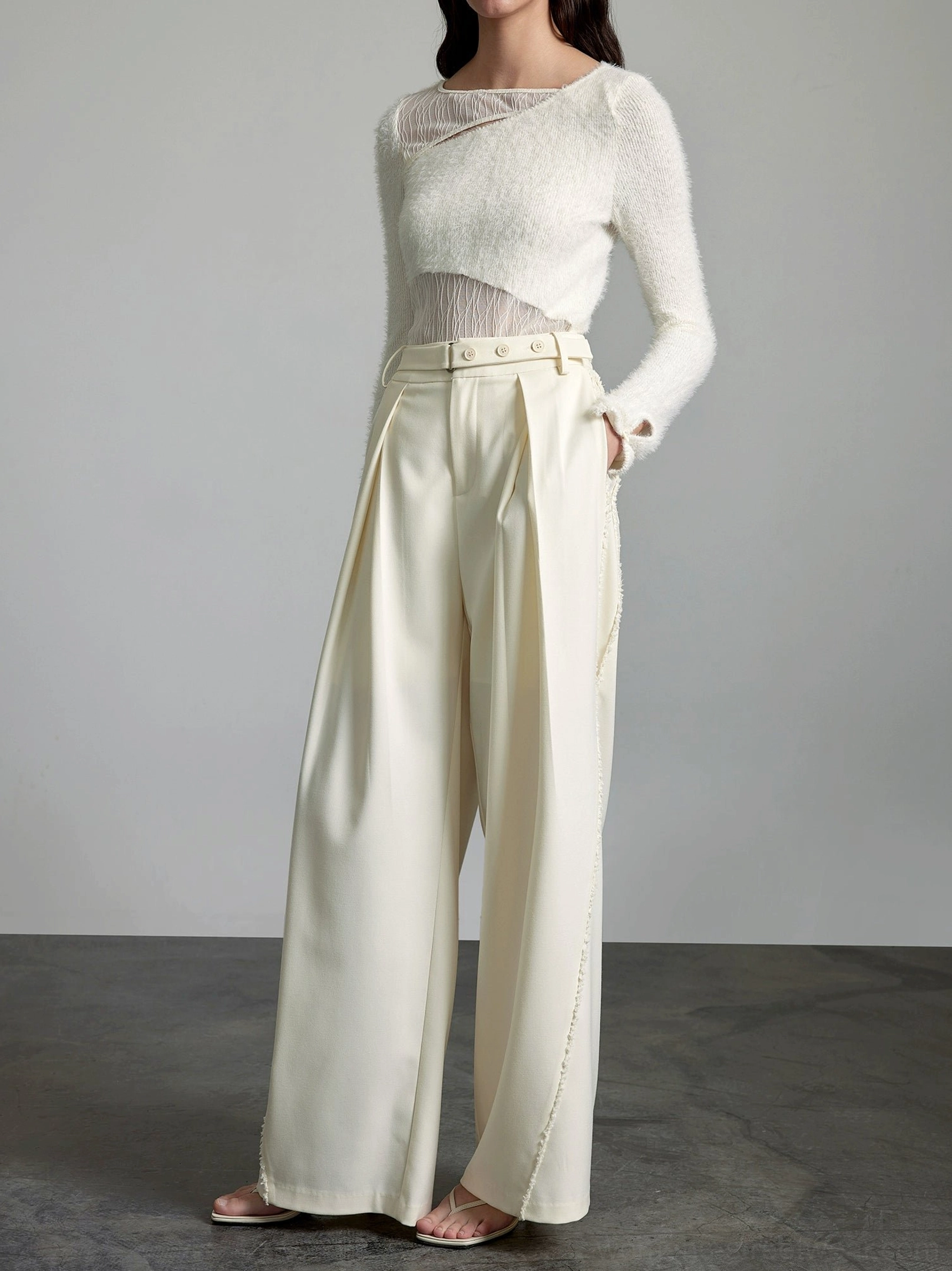 Front three-quarter view of cream high-waisted wide-leg streetwear trousers with pleats, belt loops, and tailored silhouette