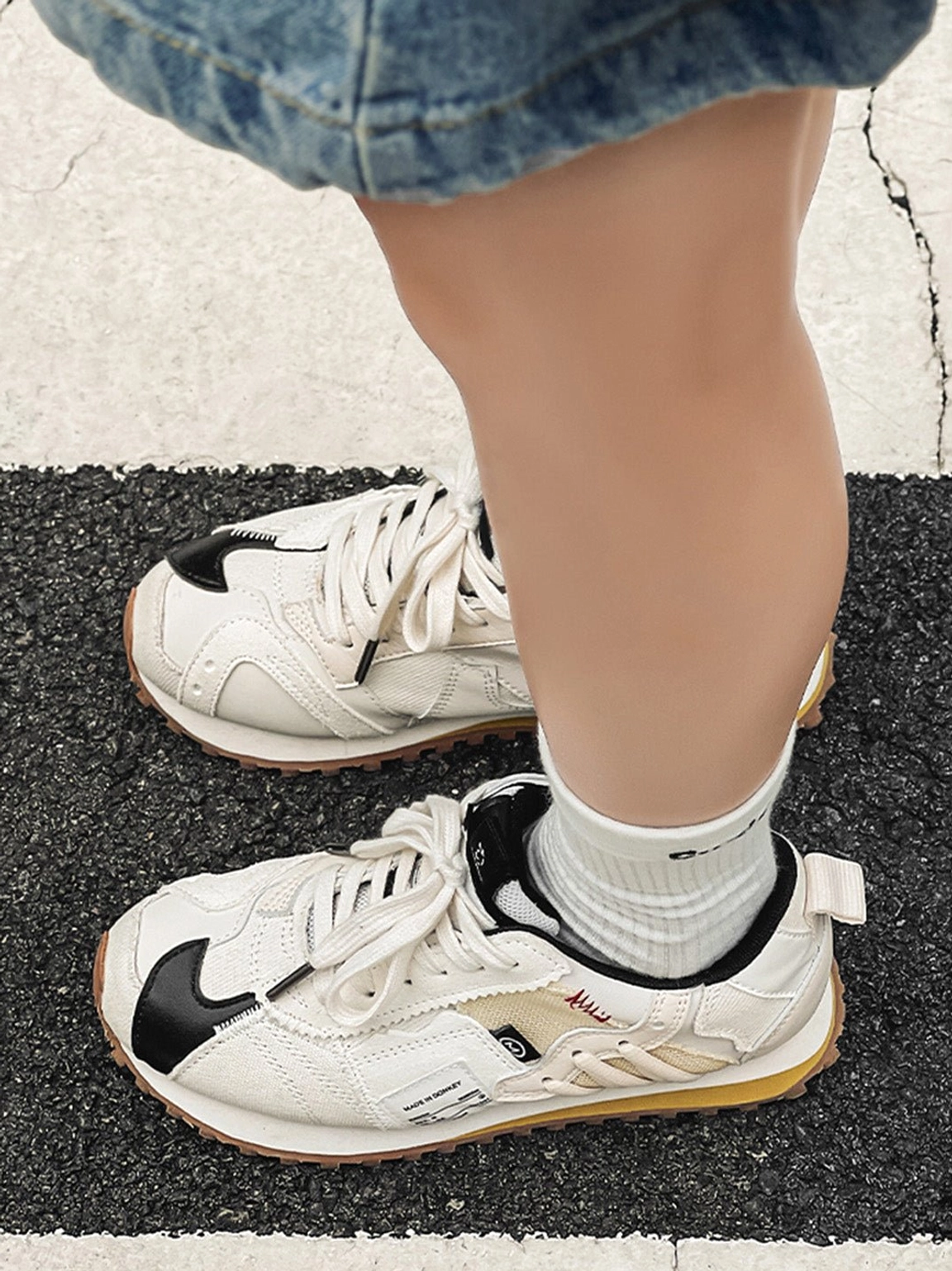Cream ivory retro runner sneaker worn beside a matching shoe on an asphalt road with visible black accents and gum outsole