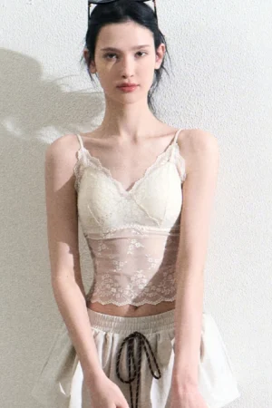 Front view of a cream lace sheer camisole top styled with a matching mini skirt in a minimalist studio