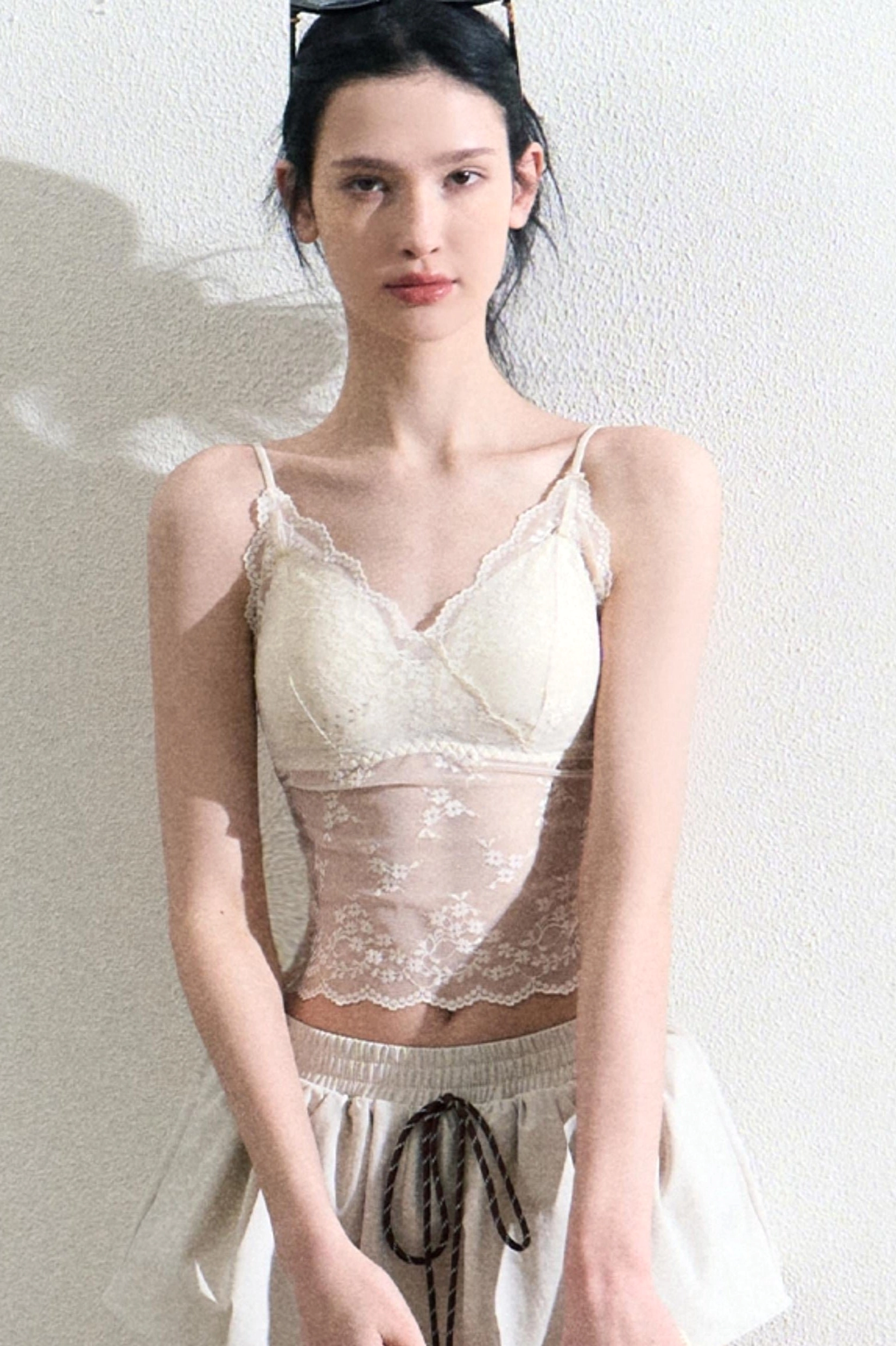 Front view of a cream lace sheer camisole top styled with a matching mini skirt in a minimalist studio