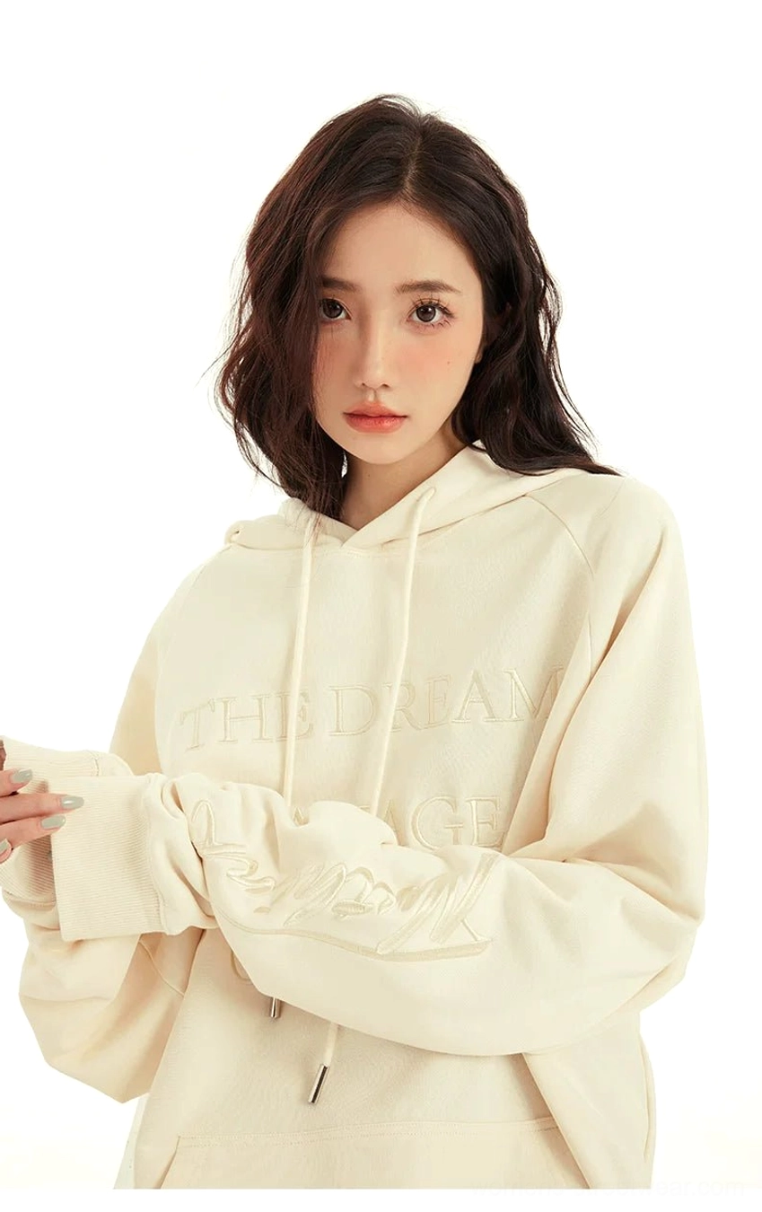 Close front view of a cream oversized hoodie featuring raised tonal lettering on the chest and sleeve with adjustable drawstrings