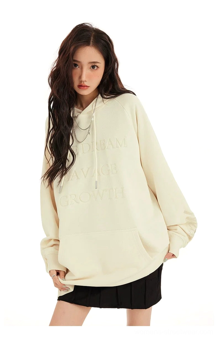 Cream oversized longline hoodie with tonal embossed chest lettering and drawstring hood styled with a pleated skirt