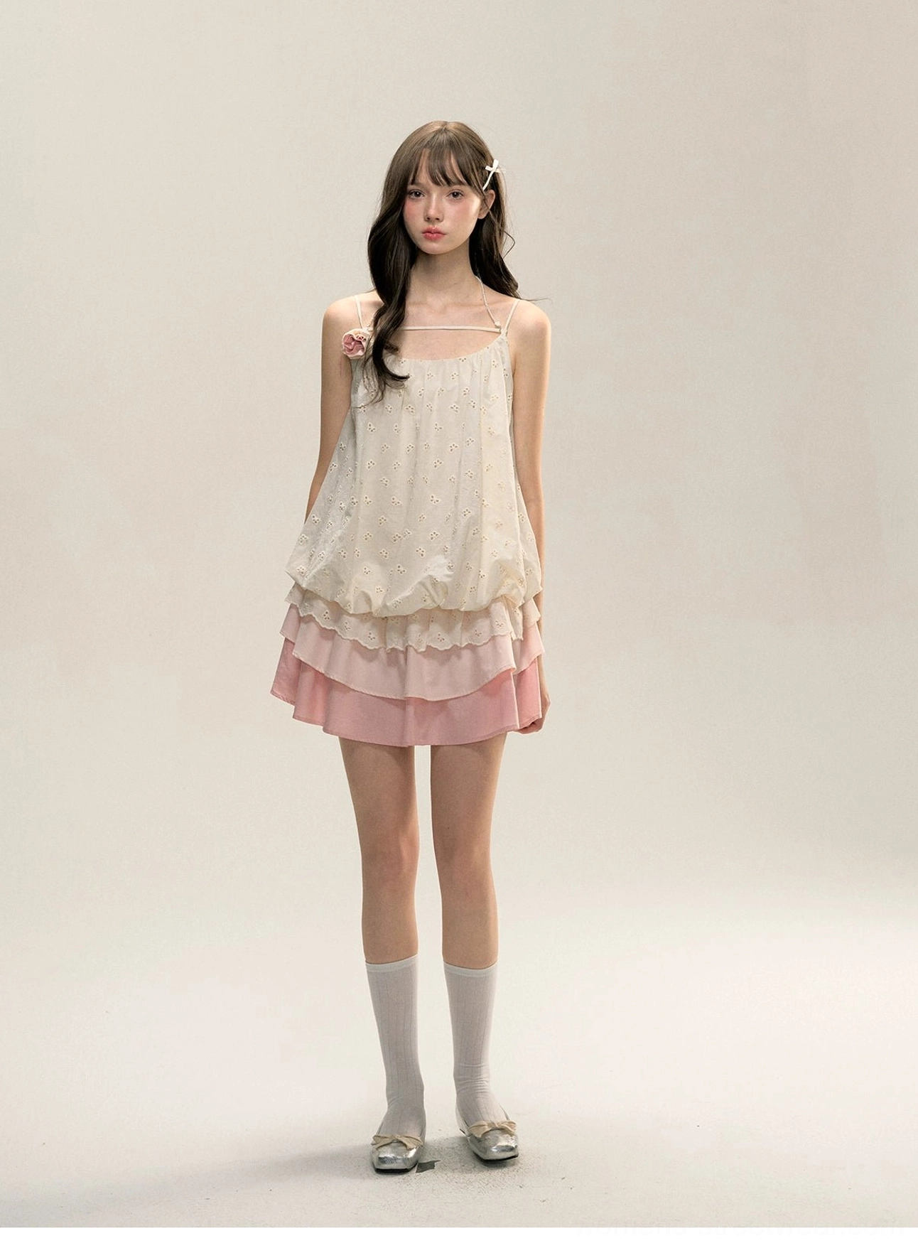 Front view of cream and pink floral tiered ruffle mini slip dress with embroidered bodice, spaghetti straps, fabric flower detail, white socks, and silver flats