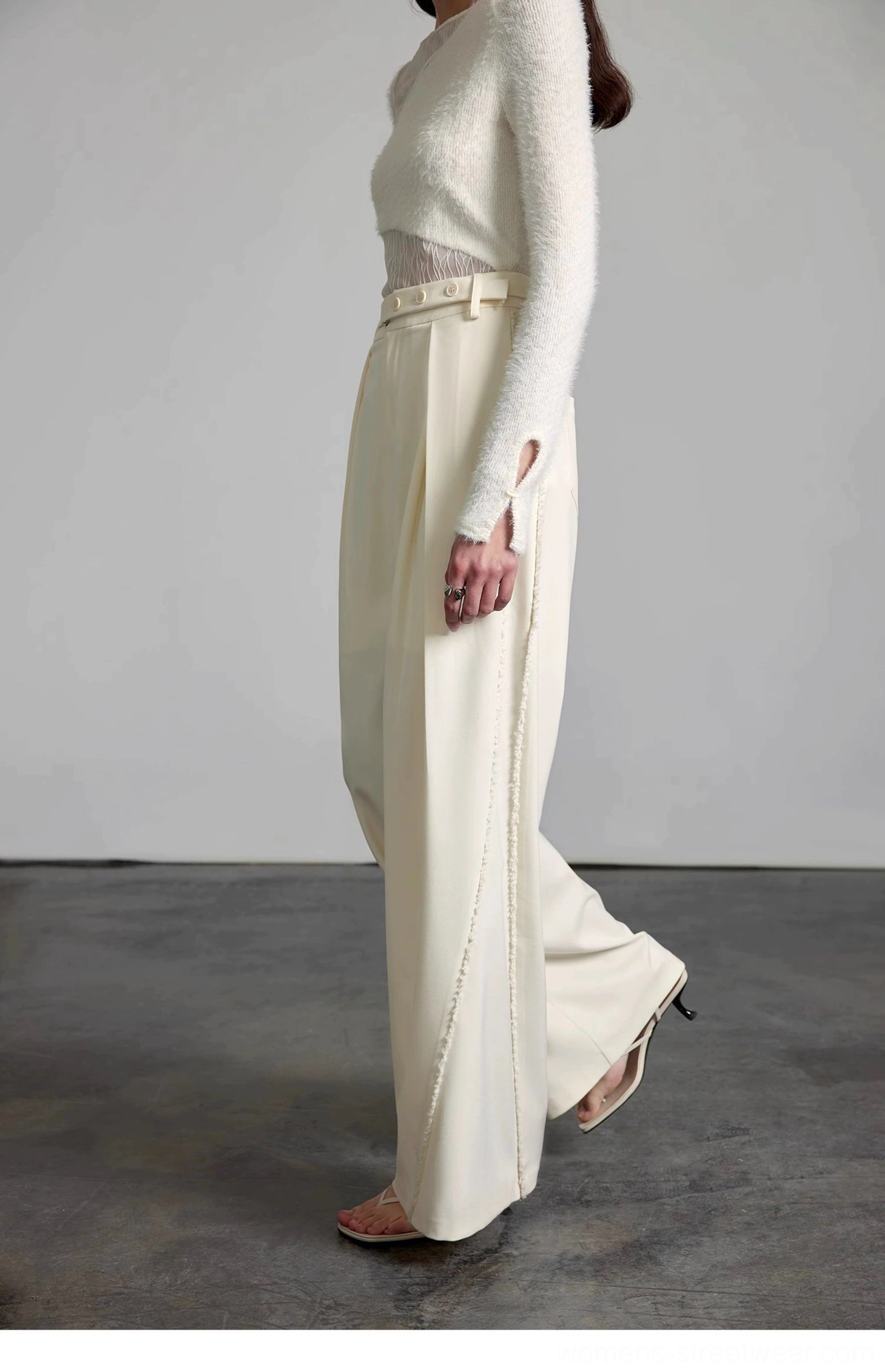 Side walking view of cream pleated wide-leg streetwear pants styled with heeled mule sandals