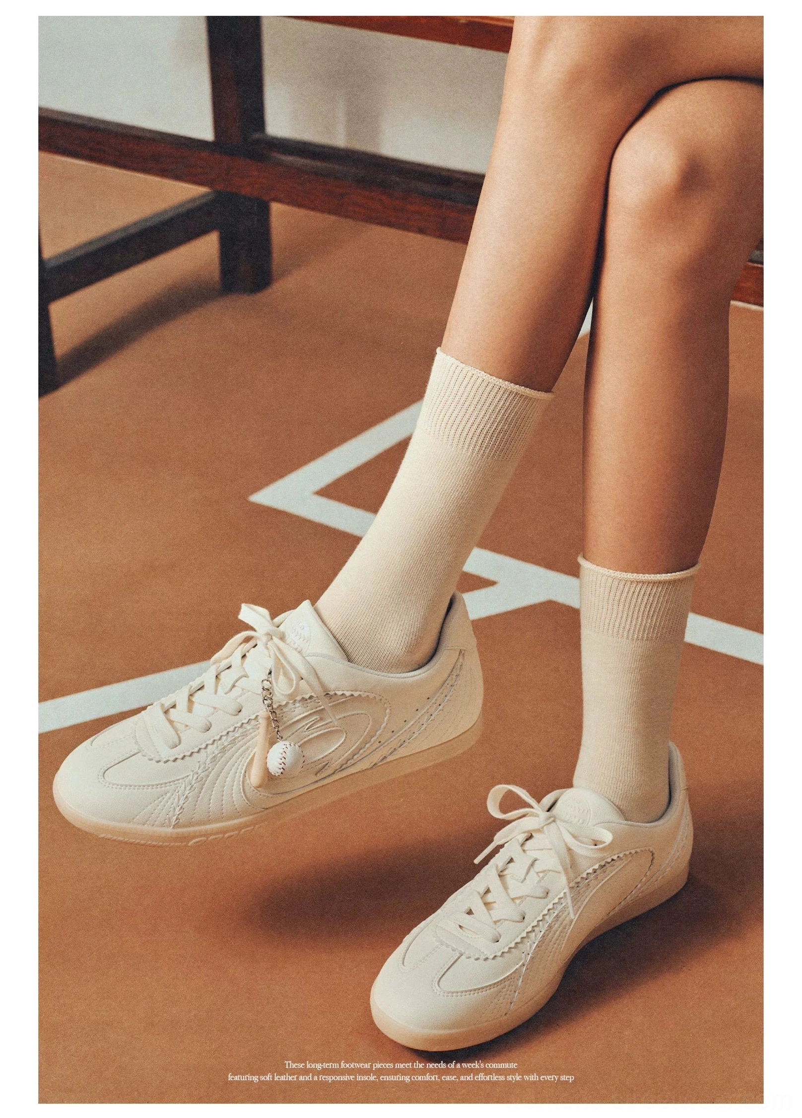Cream retro athletic training sneakers with oval side detail and gum soles on indoor court floor