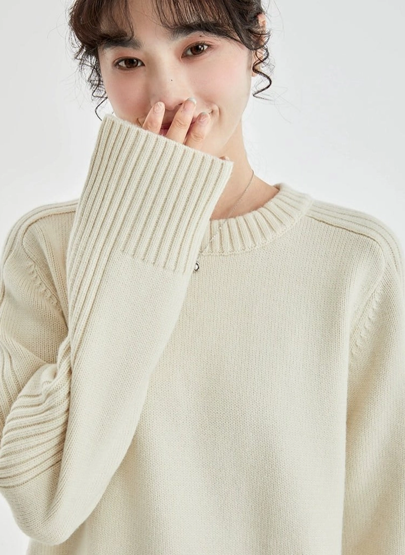 Close-up detail of the cream ribbed crewneck sweater showing the soft knit texture, wide ribbed cuffs, and drop shoulder seams