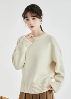 Front three-quarter view of a cream ribbed drop-shoulder crewneck sweater styled with a brown pleated midi skirt in minimalist Korean streetwear fashion