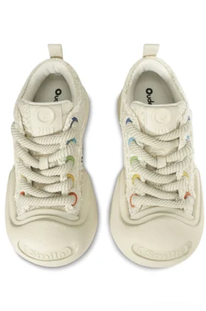 Front overhead view of cream textured canvas sneakers with thick woven laces, reinforced rubber toe caps, and playful casual streetwear details