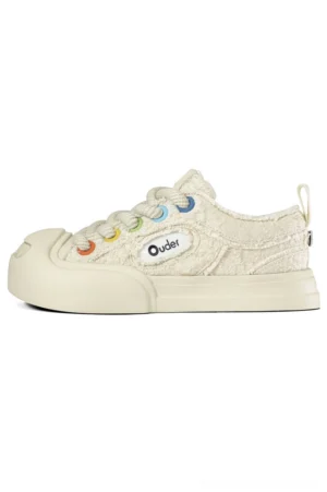 Side profile of cream textured low-top canvas sneakers with colorful rainbow eyelets, rubber sole, heel pull tab, and casual streetwear design