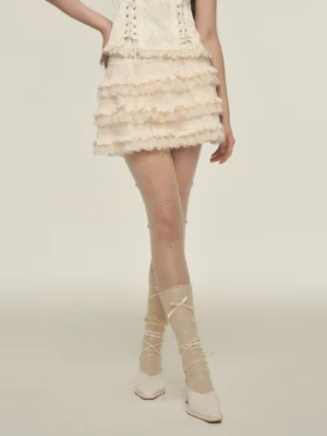 Cream tiered ruffle lace mini skirt styled with lace-up mid-calf socks and sheer rhinestone stockings in a studio fashion look