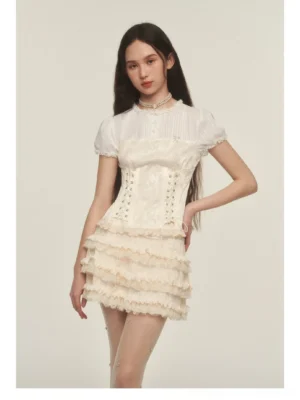 Model wearing a romantic cream ruffle mini skirt outfit with a puff sleeve corset top and pearl choker necklace