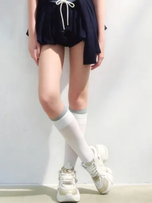 Cream white and gold chunky dad sneakers styled with dark drawstring shorts and knee-high white socks