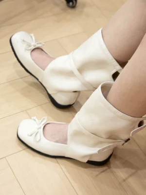 Cream white mid-calf ballet boots worn with a foldable shaft, front bow accent, ankle cutout, and comfortable flat sole
