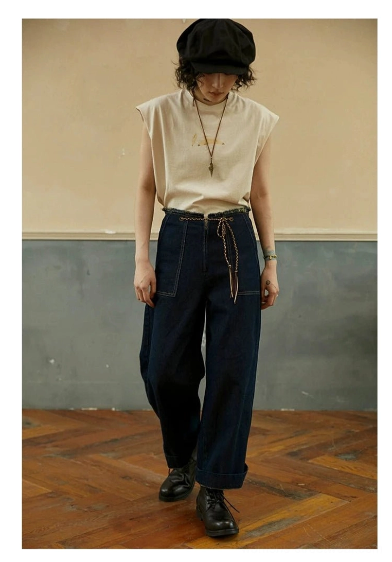 Cream White relaxed fit sleeveless streetwear tee worn with loose denim pants and leather boots in a studio setting